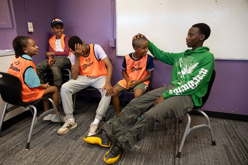 Five students wearing soccer jerseys hanging out in a classroom. 