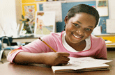 School age girl of color smiling at her desk in a classroom