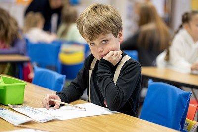 Boy in classroom looking pensive at the camera, head on hand, other students in background