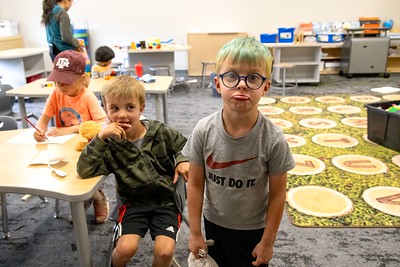 Kids in a classroom, some making silly faces, with teacher in background