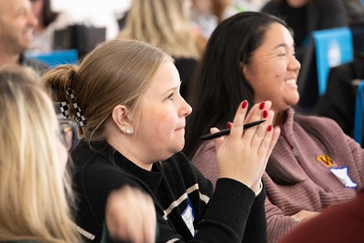 Educators at a meeting, one person in background laughs, another person in foreground is concentrating with hands clasped