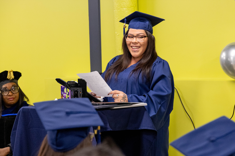 A woman in a blue cap smiles while holding notes at a podium.