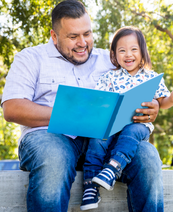 Father and young child reading a book and smiling.