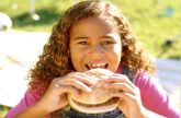 School age girl smiling and eating a hamburger outside